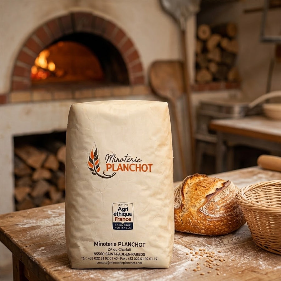 Sac de farine Minoterie Planchot posé dans une boulangerie, à côté d'un pain de campagne