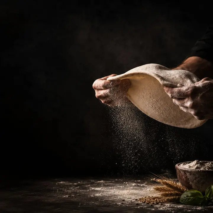 Mains étirant une pâte à pizza dans un nuage de farine